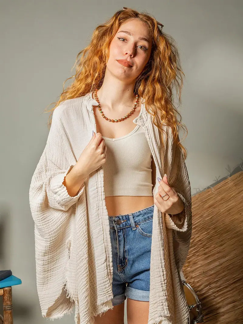 Woman wearing a beige cardigan over a white top and blue shorts, standing against a neutral background.