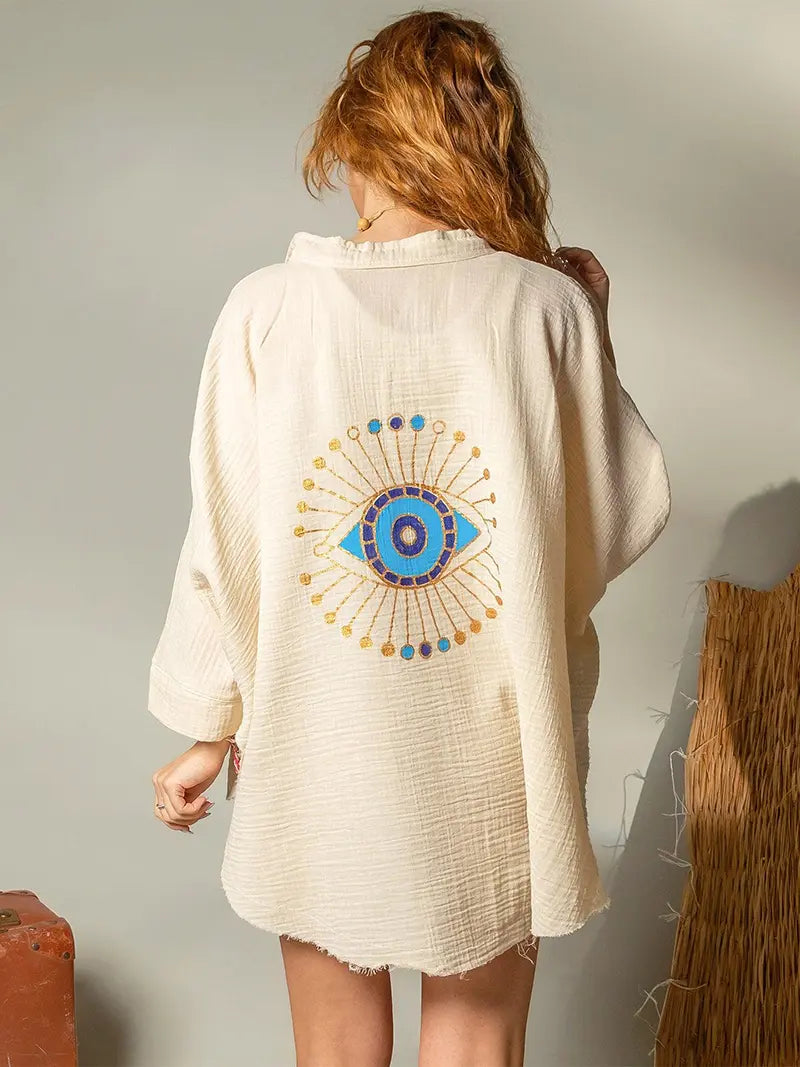 Person wearing a beige kimono-style garment with a decorative blue eye design on the back.