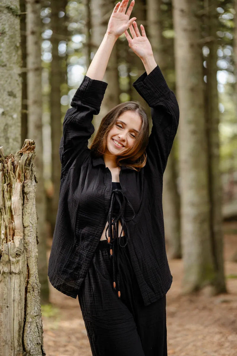 Woman in a black muslin loungerwear standing in a forest with trees in the background