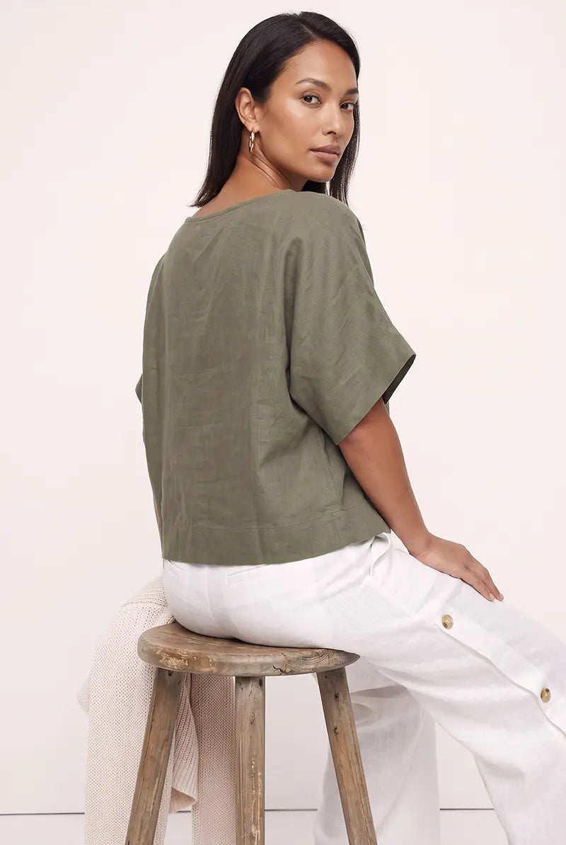Back view of the olive green linen blouse top, seated on a wooden stool