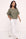 A woman modeling a short-sleeve olive green top and white wide-leg pants with gold-tone side buttons, standing against a plain off-white studio background.