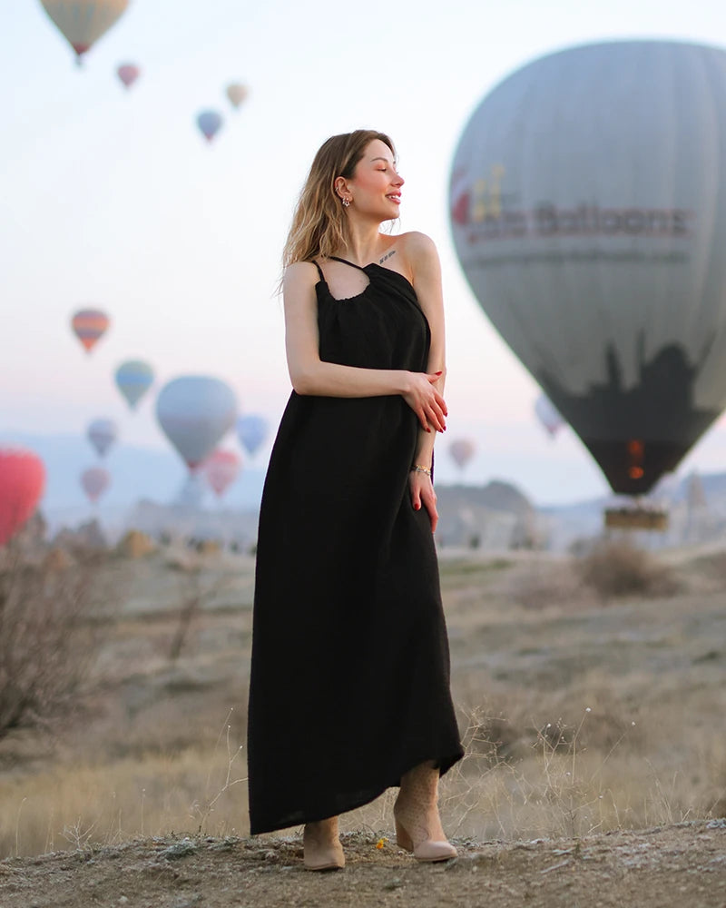 Woman in a black double gauze evening dress standing in front of hot air balloons