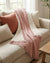 Pink muslin throw blanket on a beige sofa with cushions in a cozy living room.