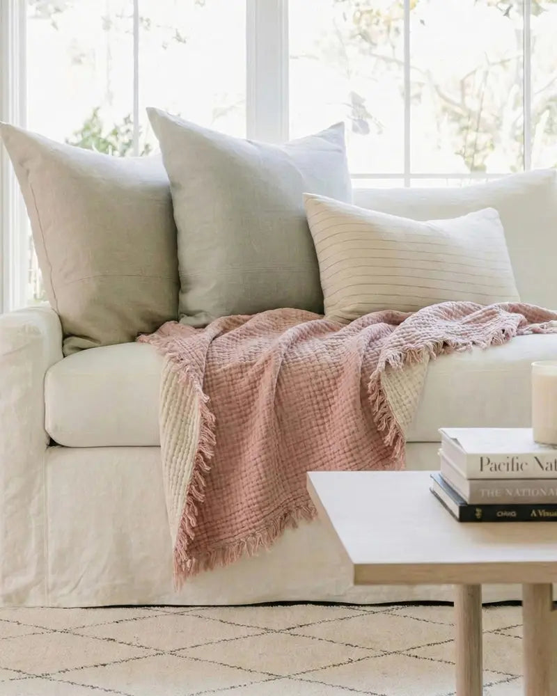 Beige sofa with pink throw blanket and white pillows in a bright room.