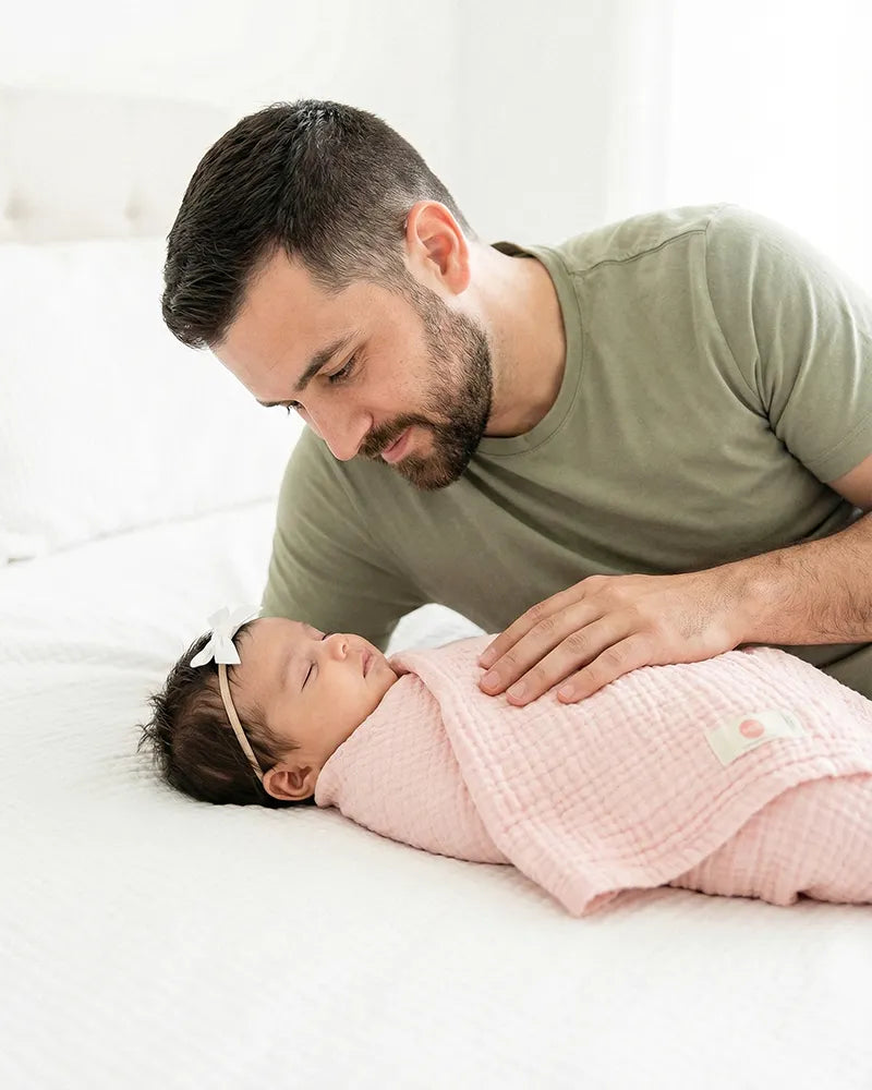 Man lying next to a baby wrapped in a pink blanket on a white surface