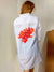 White shirt with red coral design on the back, worn by a person against a plain background