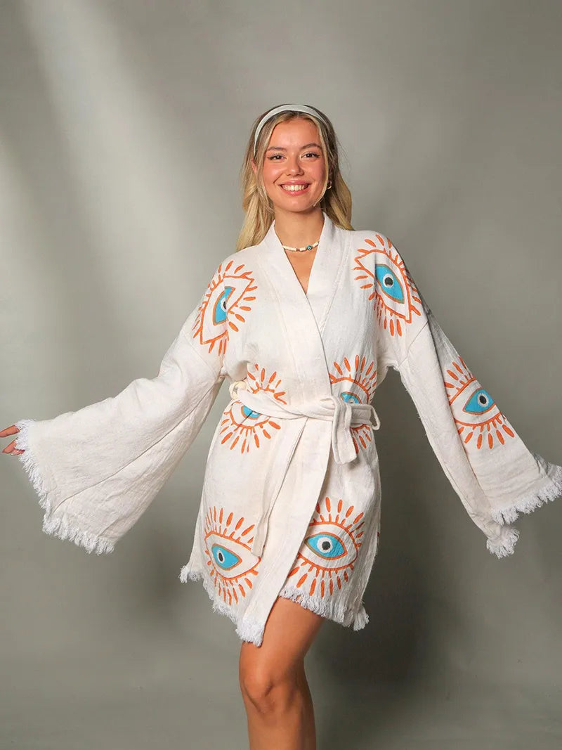 Woman wearing a white robe with eye designs on a gray background