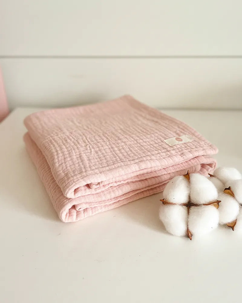 Folded pink baby blanket with cotton fibers on a light surface