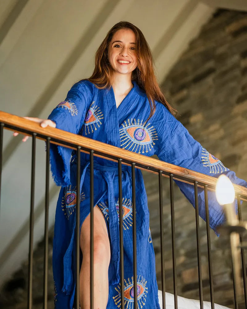 Woman wearing a blue kimono with evil eye design standing on a staircase.