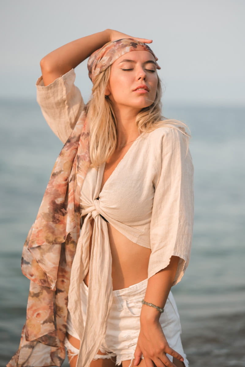 Woman on a beach wearing a beige linen front tie crop top with a scarf