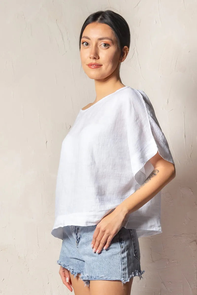 Woman wearing a white short sleeve linen top and denim shorts against a plain background