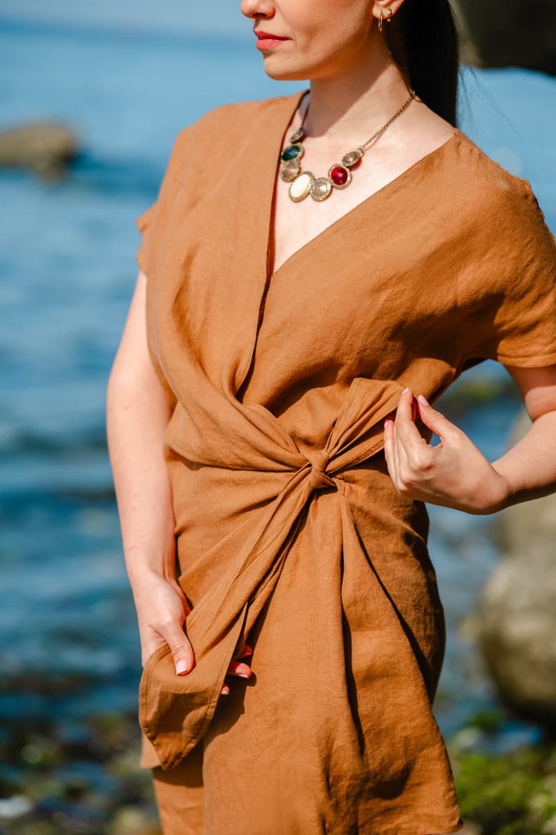 Woman wearing a brown linen wrap dress with a blurred natural background