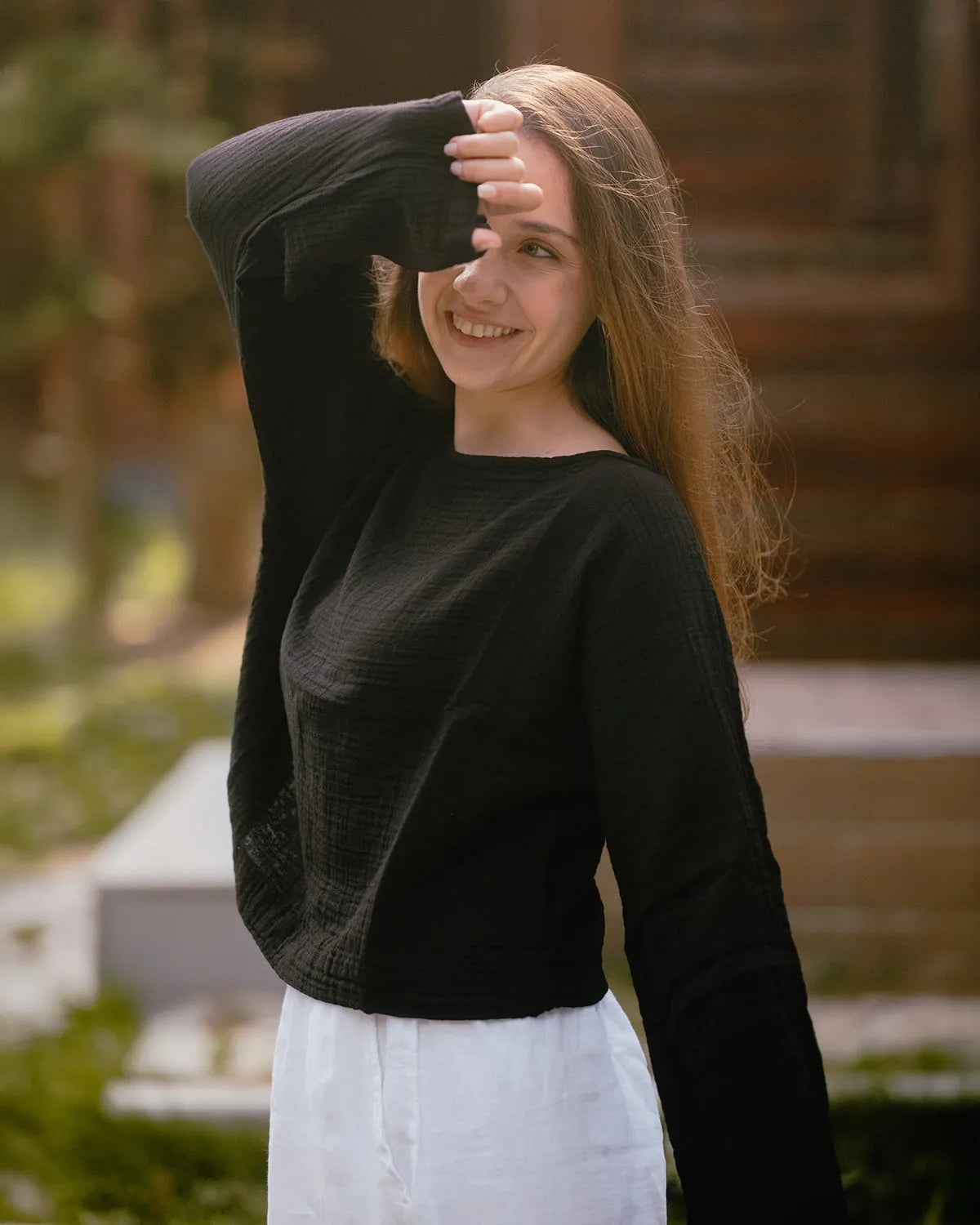 Woman wearing a black crinkle cotton long sleeve top and white linen pants outdoors