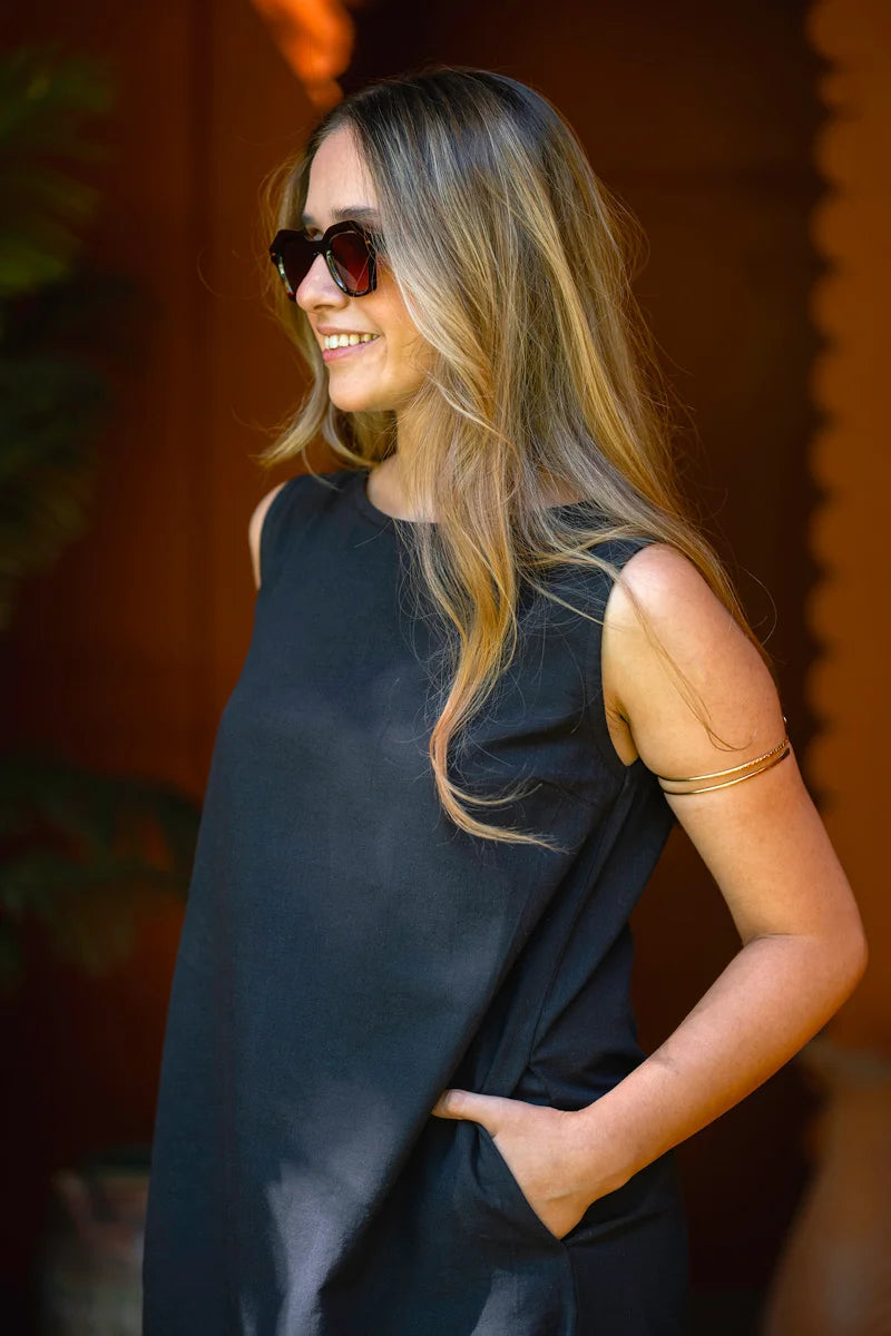 Woman wearing a black sleeveless a line dress with sunglasses on a blurred background