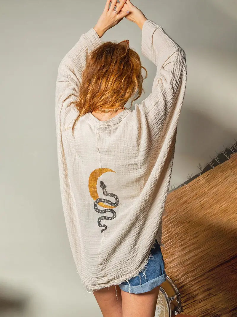 Person wearing a beige double gauze cardigan with a crescent moon and snake design, standing against a neutral background.