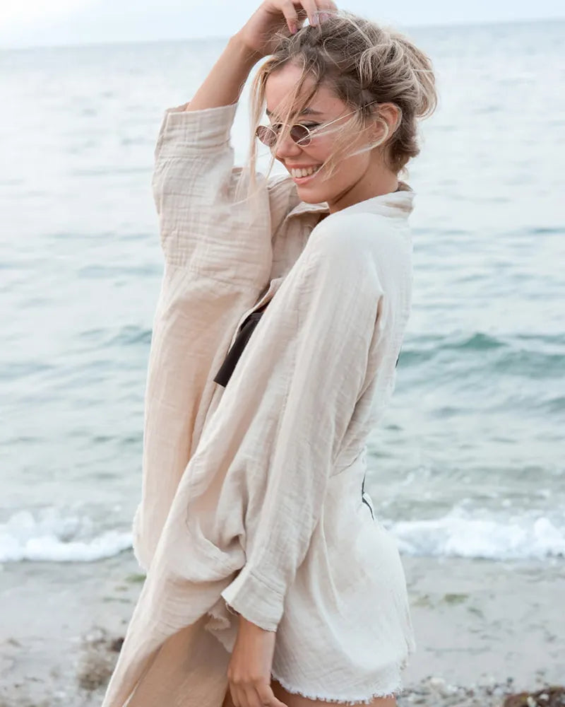 Woman in a cream cardigan standing on a beach with ocean waves in the background