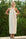 Woman wearing a striped dress with a halter neck design, standing outdoors with greenery in the background.
