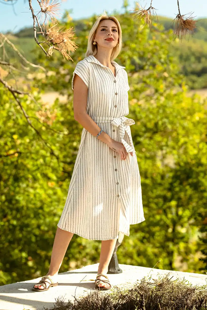 Woman in a belted midi dress standing outdoors with greenery in the background