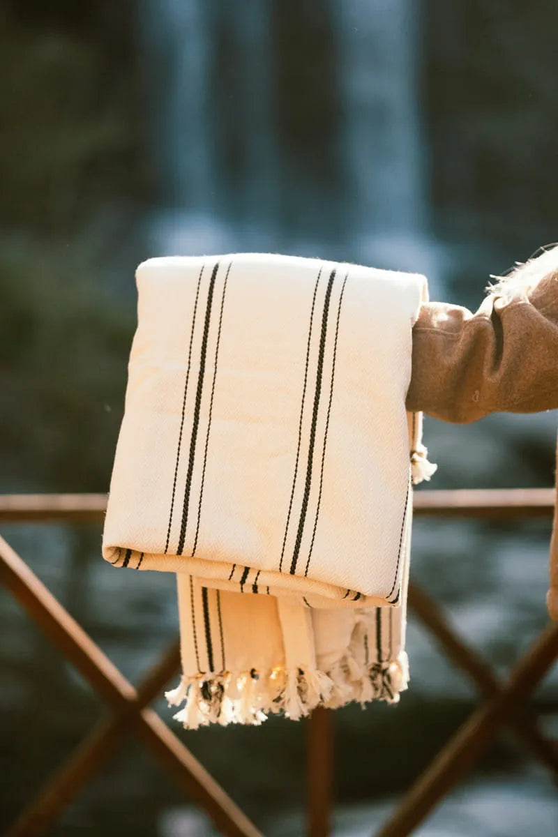 cream blanket with black stripes held by a person against a blurred natural background