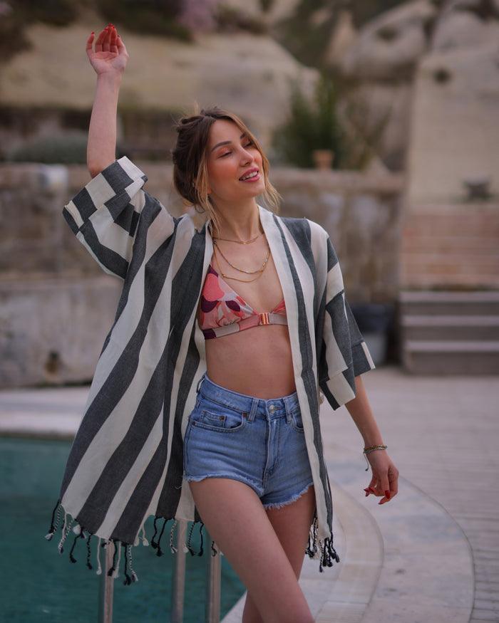 A woman stands by a pool, dressed in a Turkish robe with stripes