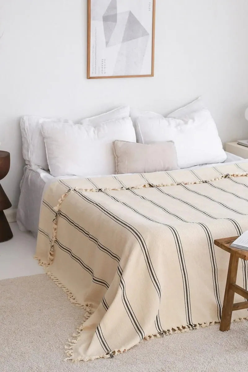 cream striped blanket on a bed in a bedroom with a white wall and framed abstract art.