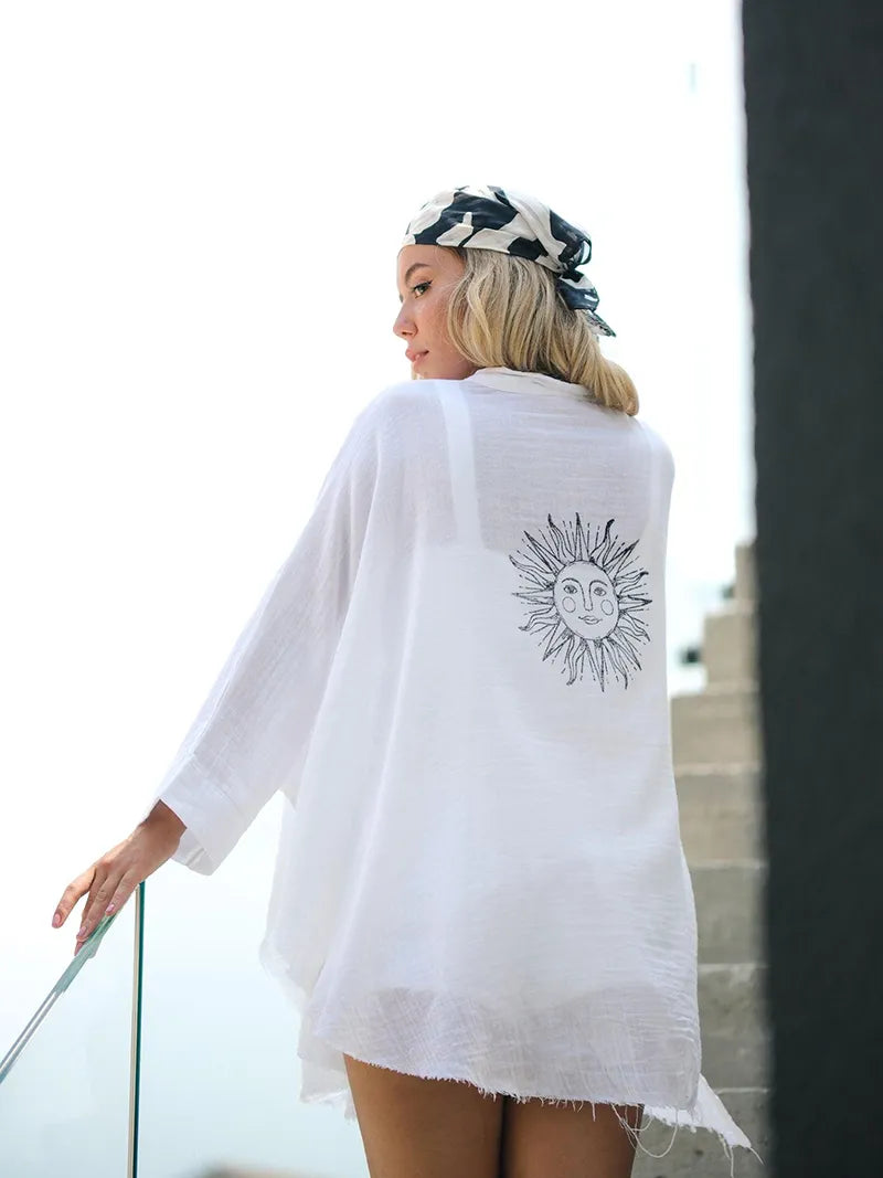 Woman wearing a white cover-up with a sun design on a balcony.
