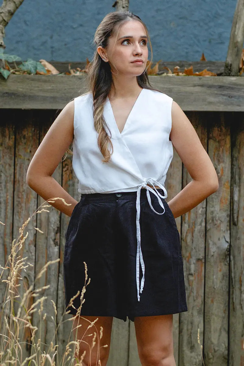 Woman wearing a white sleeveless   vest top and black shorts standing against a wooden fence.