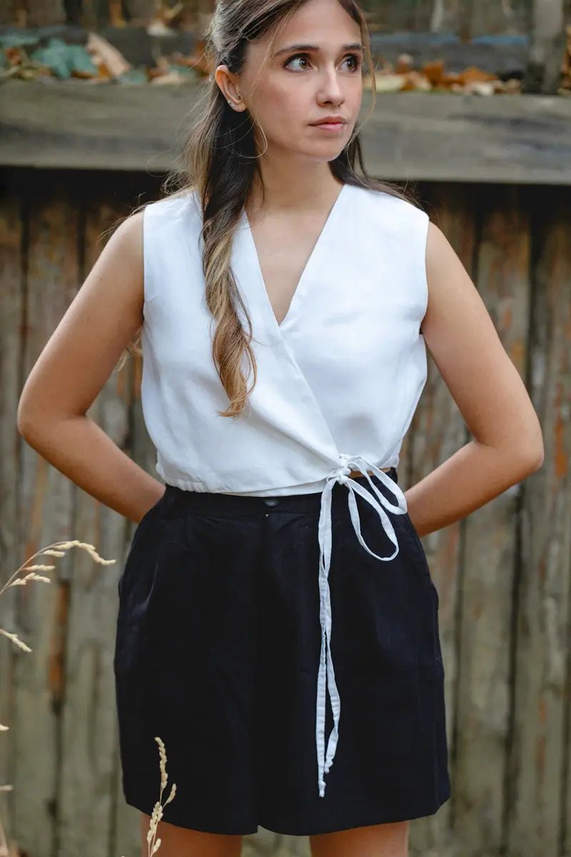 Woman wearing a white sleeveless linen tie front top and black shorts with a wooden fence background
