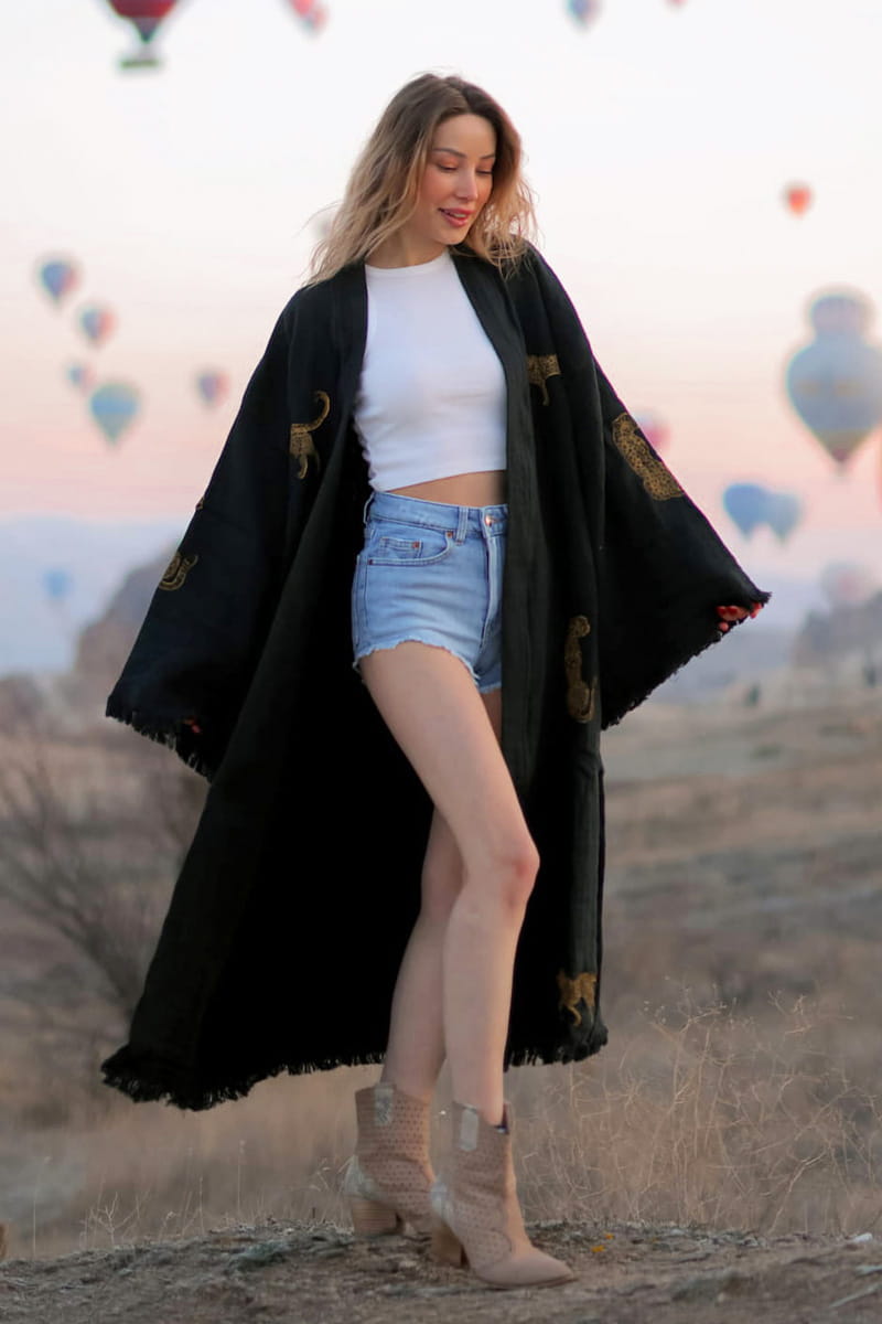 Woman in a black kimono and denim shorts standing in a desert with hot air balloons in the background