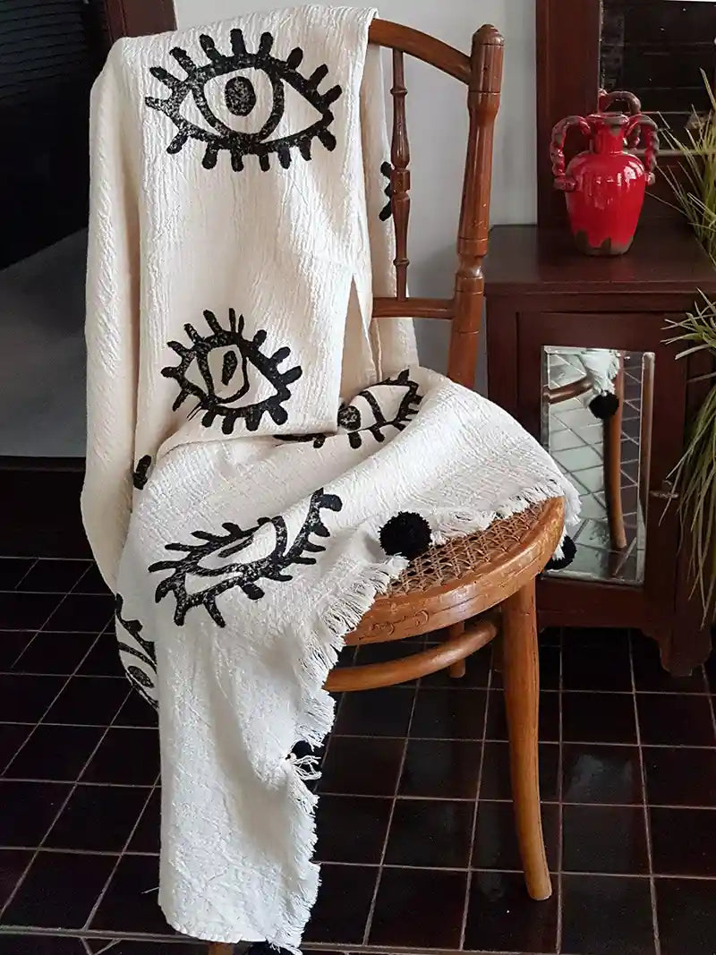 White blanket with black eye designs draped over a wooden chair in a room.