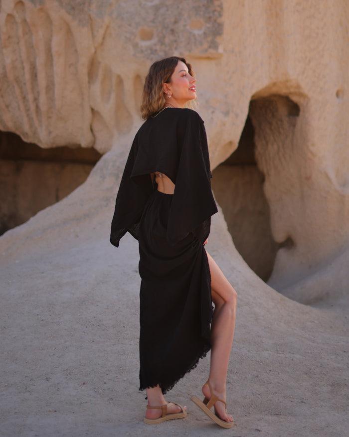 A woman wearing a black V-neck dress poses in front of a dramatic rock formation.