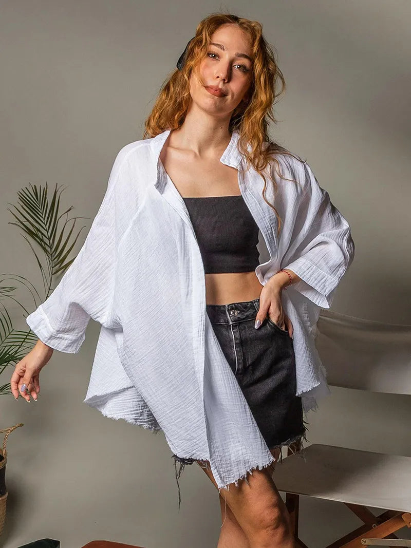 Woman wearing a white long sleeve robe over a black crop top and shorts, standing indoors.