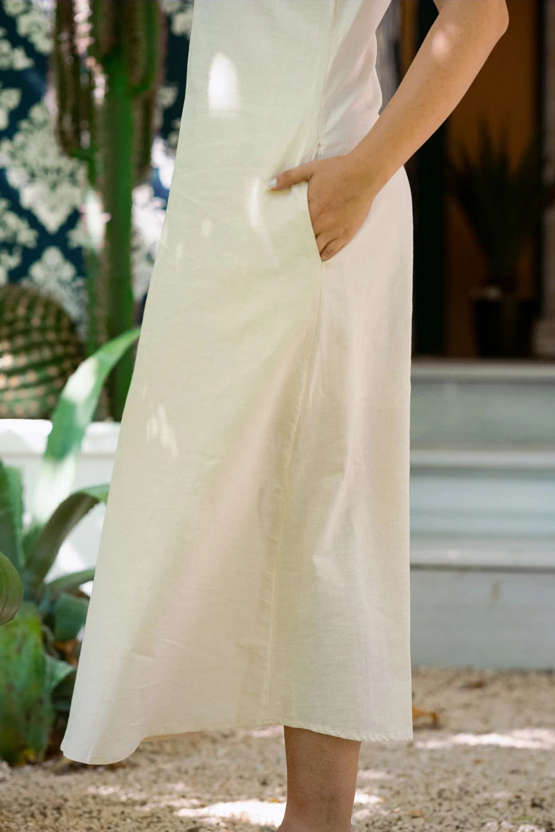 Person wearing a white dress standing outdoors with plants and steps in the background