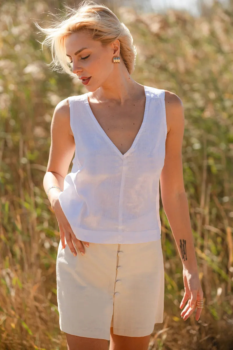 Woman wearing a white sleeveless linen top and beige shorts in a natural setting
