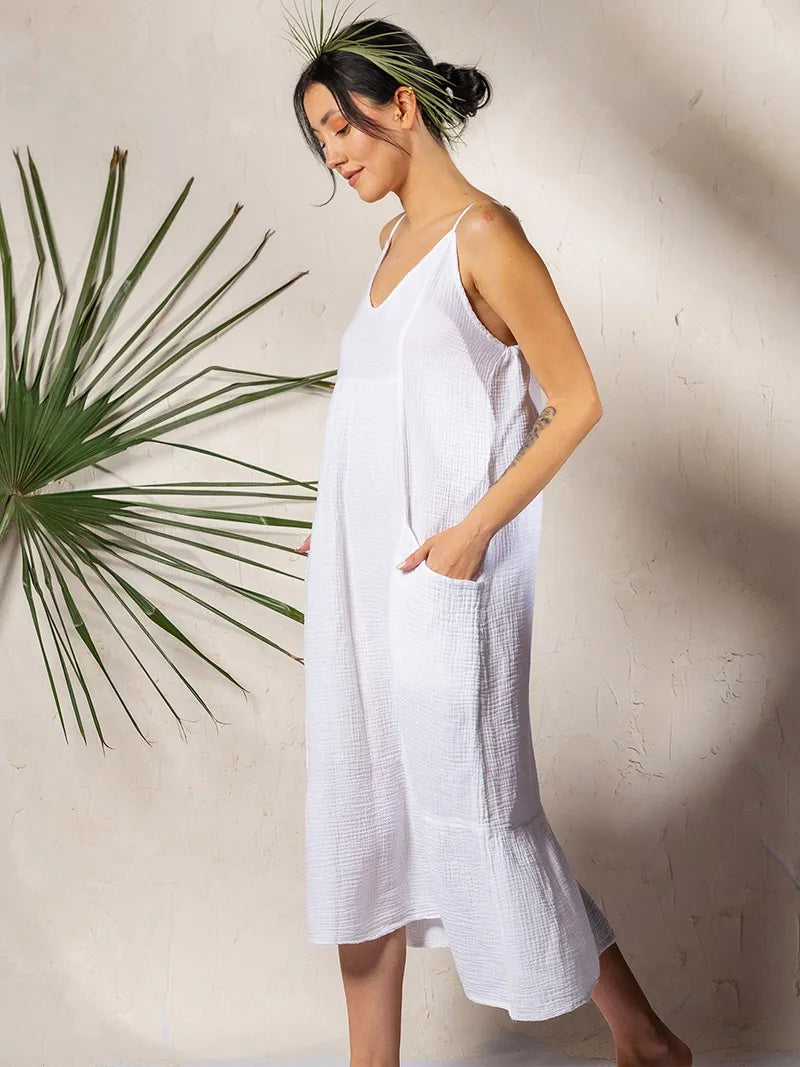 Woman wearing a white crinkle cotton midi dress standing next to a plant against a neutral wall