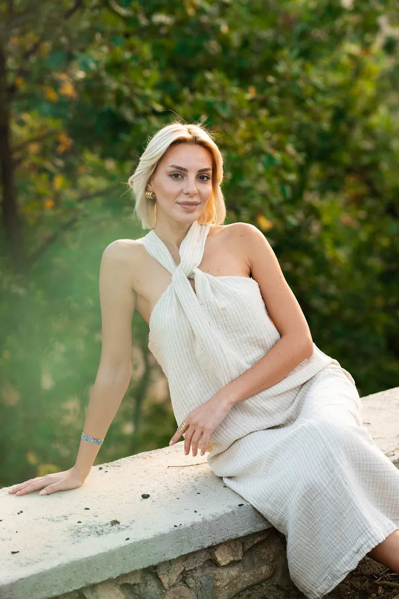 Woman in a striped halter neck dress sitting on a stone wall with greenery in the background