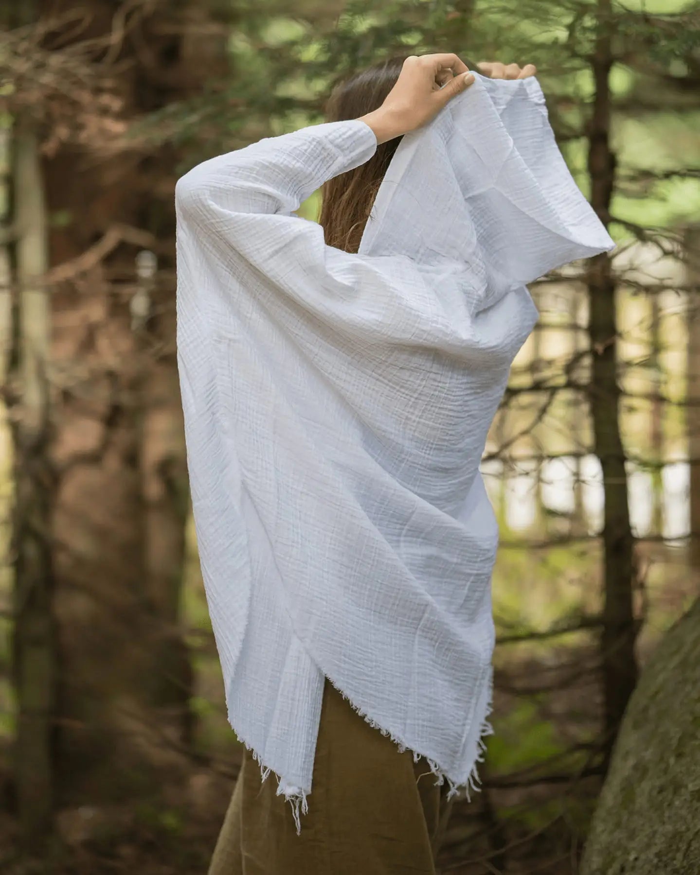Person wearing a white crinkle cotton poncho over their head in a forest setting