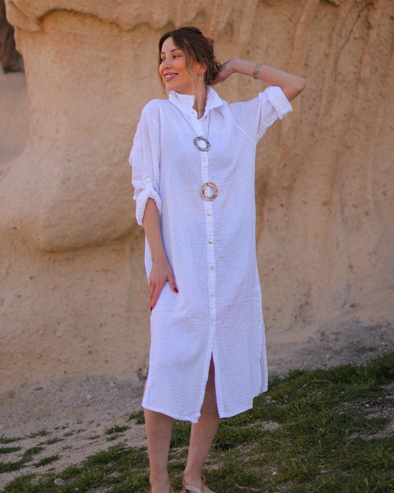 A woman standing outdoors wearing a white long sleeve dress shirt with button-down front and a collar.