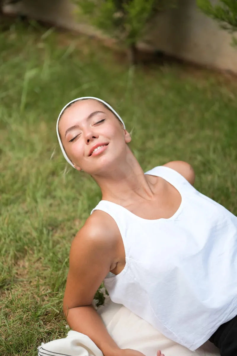 Woman lying on grass wearing a white tank top and headband