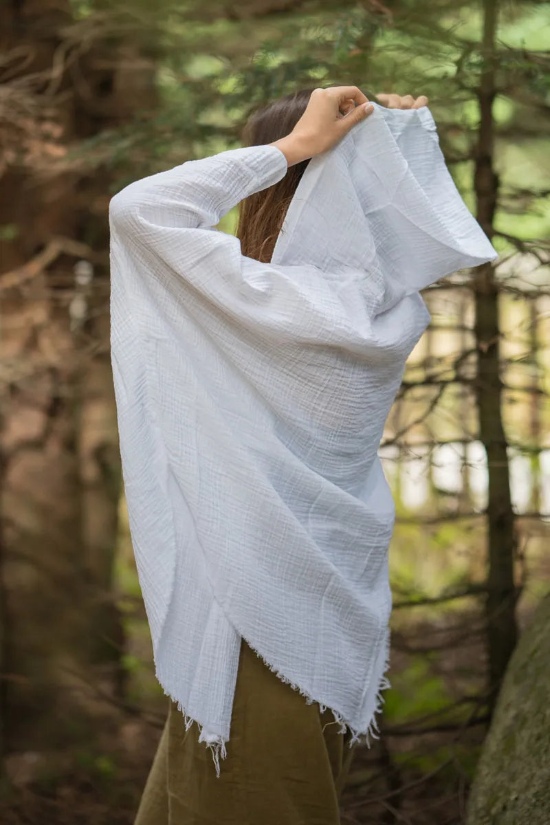 Person wearing a white muslin robe with hoodie in a forest setting