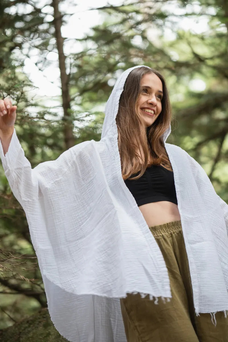 Woman wearing a white hooded muslin robe in a forest setting