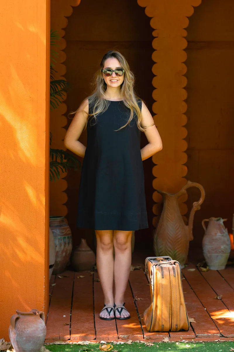 Woman in a black shift dress standing in front of an orange wall with decorative vases.