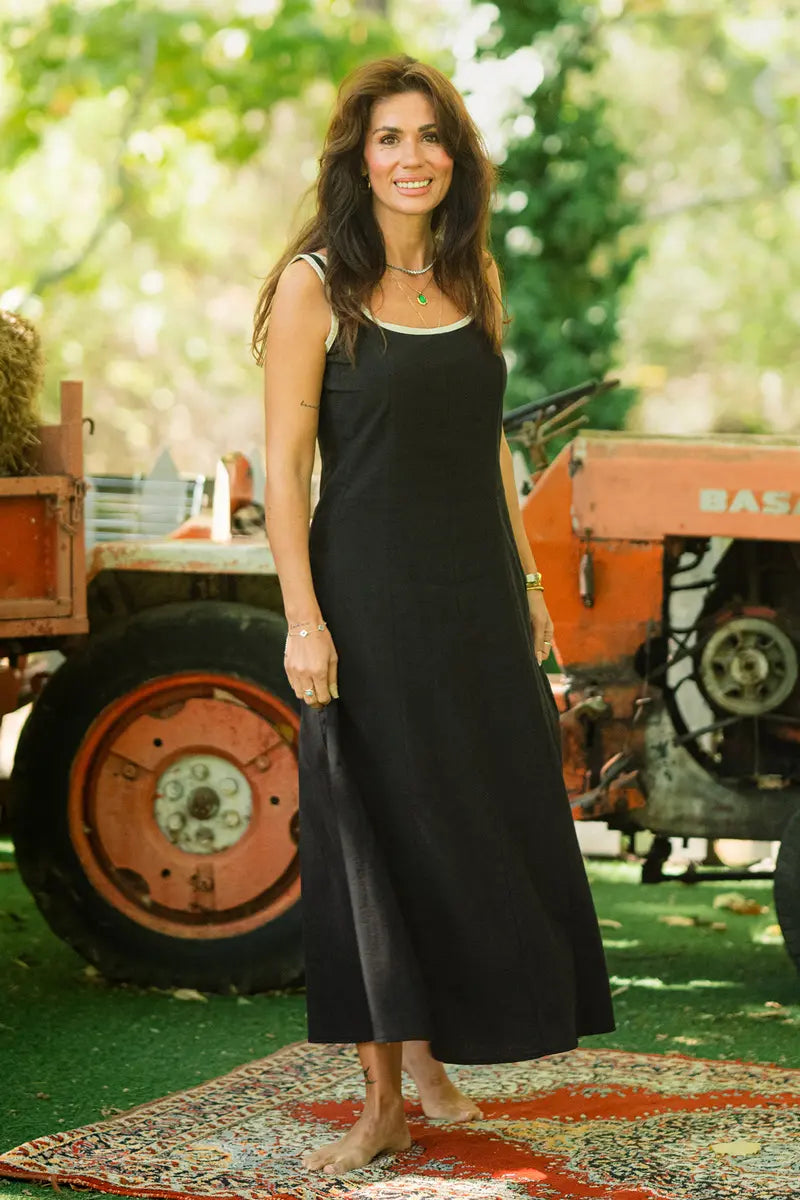 Woman in a black dress standing outdoors with greenery and vintage equipment in the background