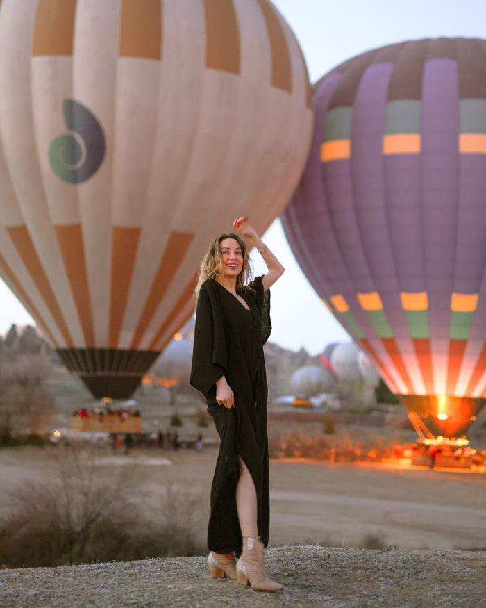 A woman in a stylish black double gauze muslin dress stands near a bright hot air balloon, enjoying a sunny day outdoors.