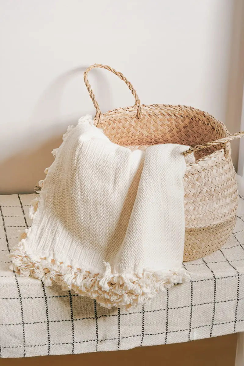 Woven basket with a cream textured cotton  blanket on a checkered surface